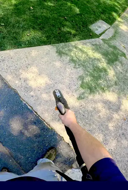 Lawn care professional using a leaf blower to clear grass clippings from a sidewalk in Charlotte, NC.