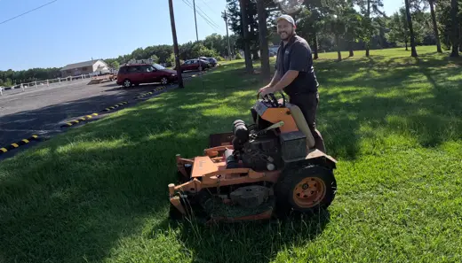 A lawn care professional mows a lush green lawn on a sunny day in Charlotte.