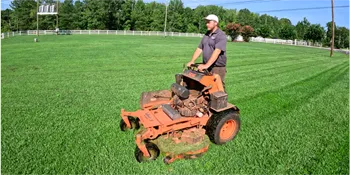 A professional landscaper in Charlotte mows a large, lush green field using a commercial riding mower.