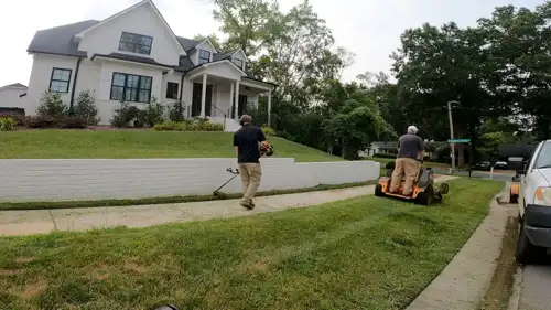 Lawn care professionals mowing and trimming grass in front of a large residential property in Charlotte, NC.