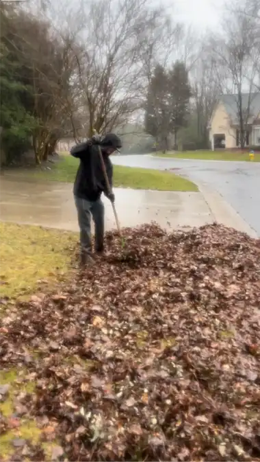 Worker raking wet leaves on a rainy day in Charlotte, NC, as part of a comprehensive leaf removal service.